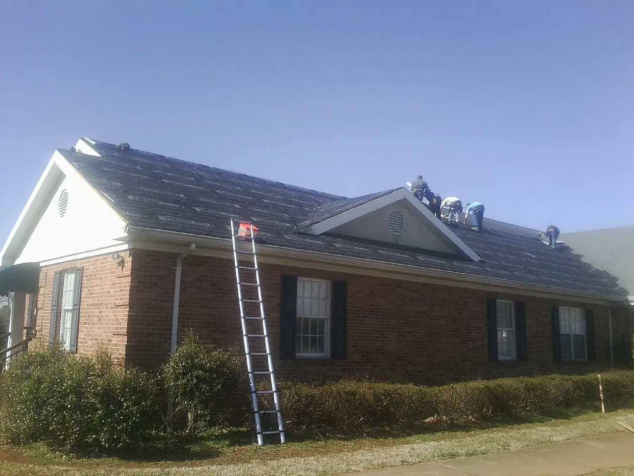 Crew tearing shingles off a brick ranch roof with a ladder set — Metal Roof Repair work by our crew in Litchfield
